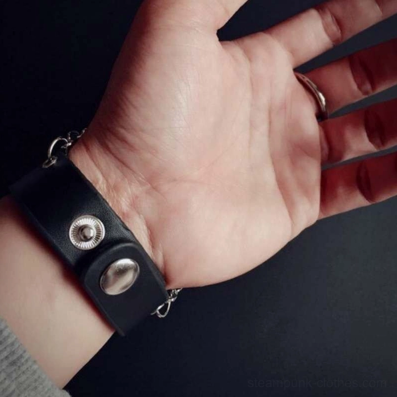 Steampunk leather bracelet strap close-up showing black leather, silver snap button fasteners, and metal chain detail on hand model