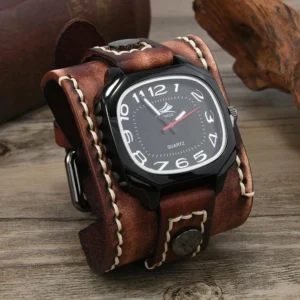 Steampunk quartz cuff watch flat lay featuring distressed brown leather strap with white topstitching, glossy black square case, raised silver numerals and red accent hand on rustic wooden table