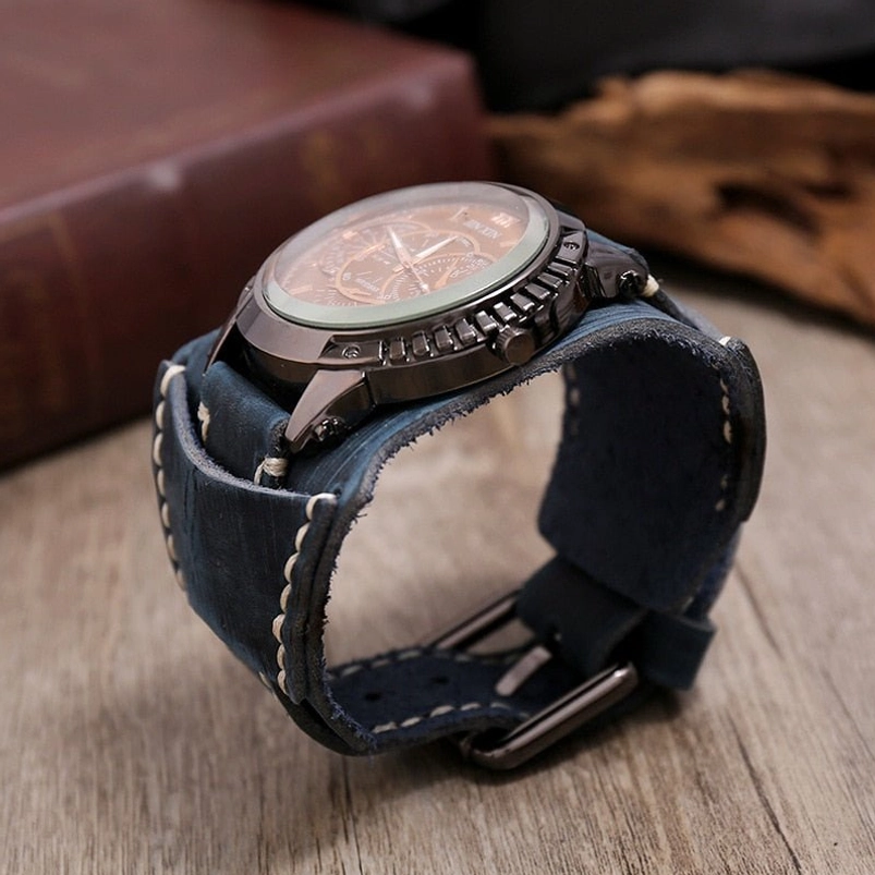 Steampunk wristwatch with dark blue leather strap and gunmetal case displayed at side angle with vintage books and wooden accessories