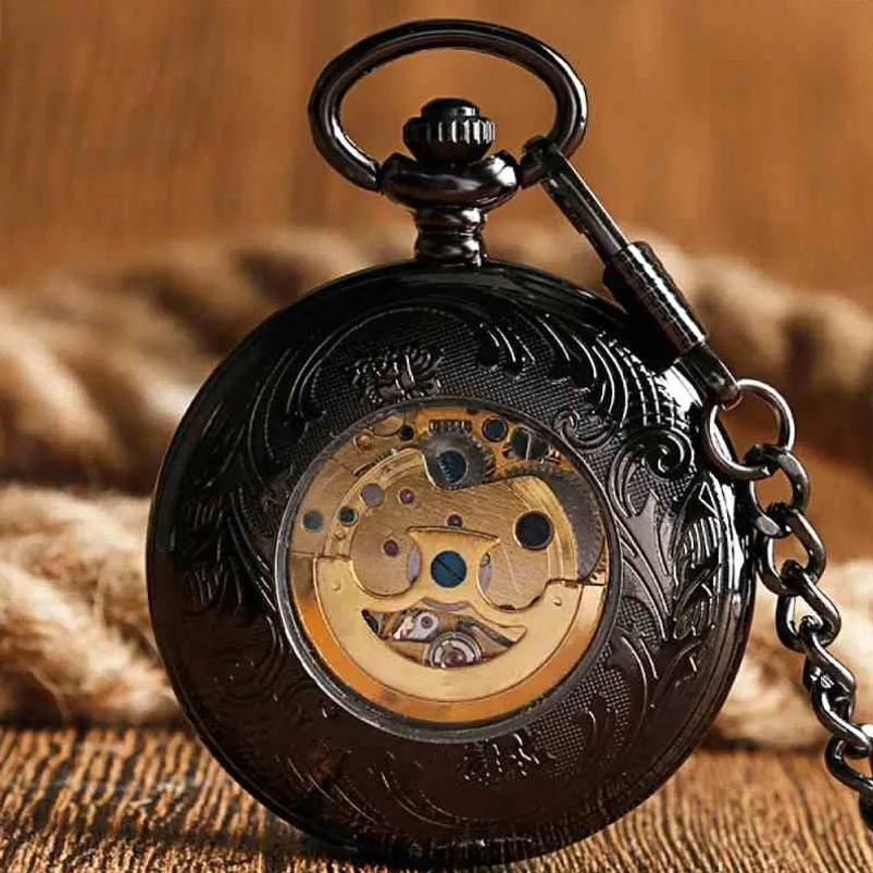 Close-up of steampunk pocket watch case featuring black engraved floral metal exterior and clear display window revealing gold internal mechanical gears