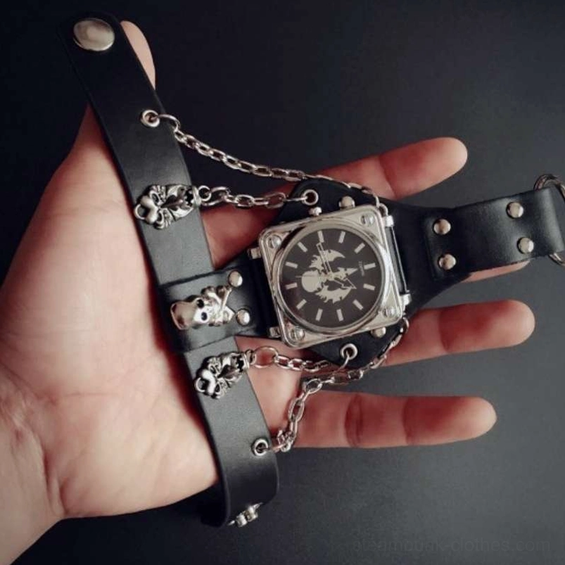 Flat lay of steampunk decorative watch displaying multiple skull charms, silver chains, and square stainless steel case on dark studio background