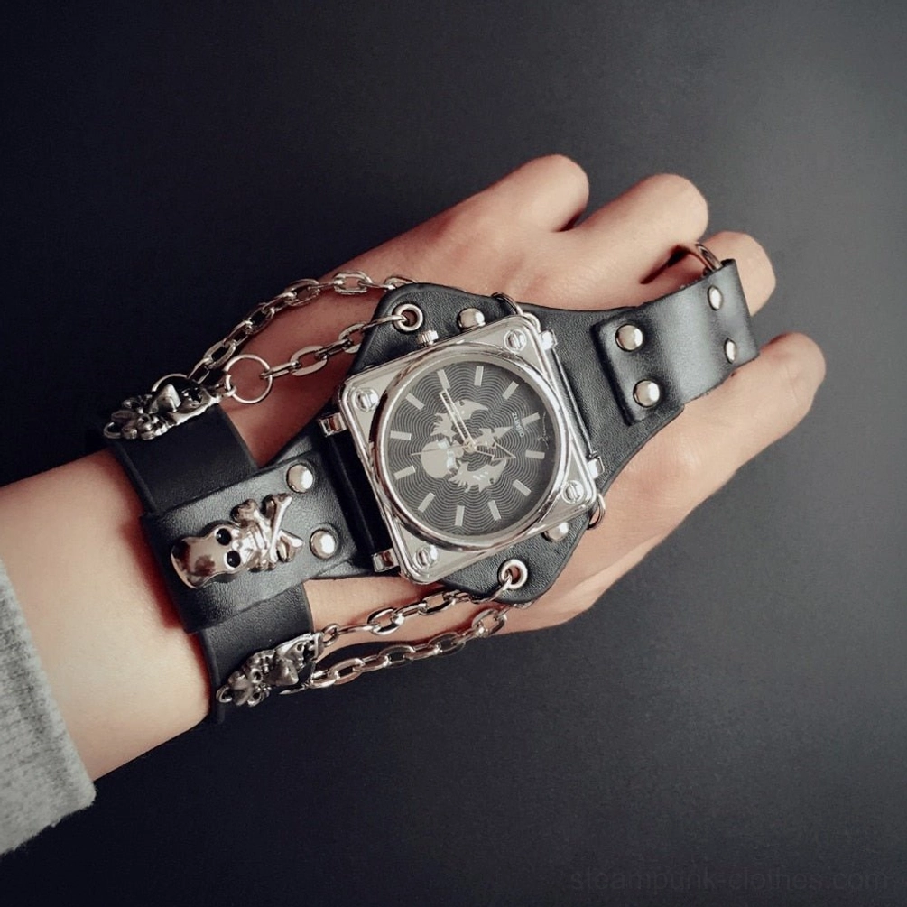 Close-up overhead view of steampunk square case watch featuring silver skull ornaments, black leather strap with snap buttons, and chain embellishments on dark background
