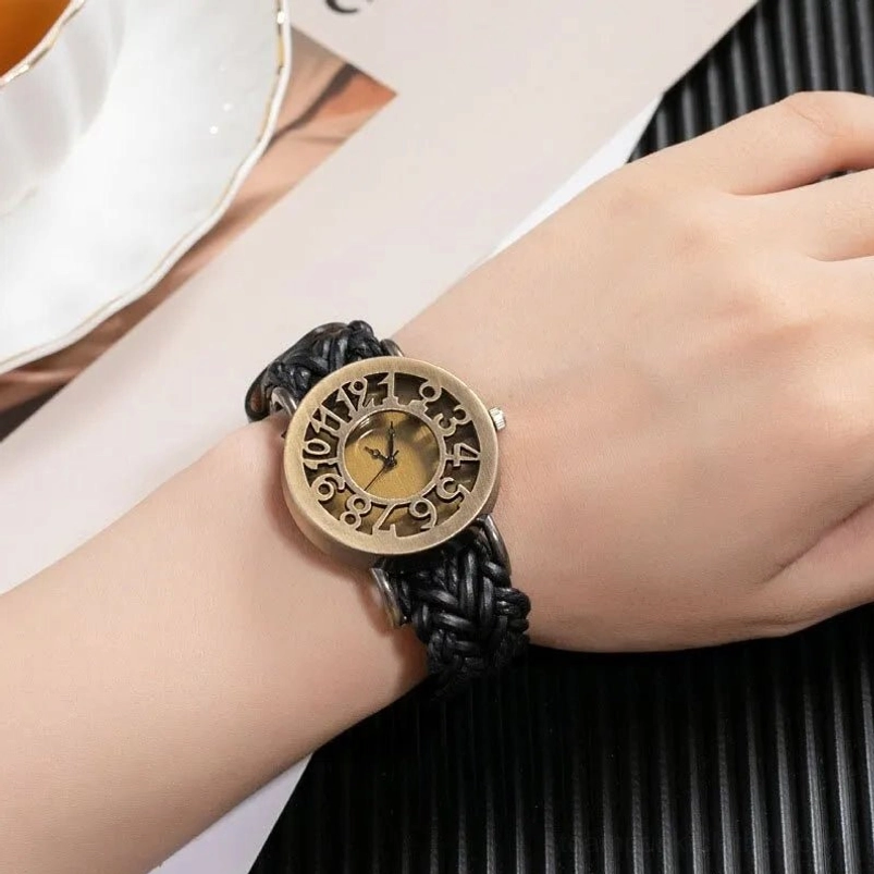 Steampunk quartz watch worn on wrist, side view displaying bronze dial and black braided leather strap with white ceramic cup in background
