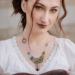 Steampunk wing gear necklace with dual metal tones worn on model in vintage lace-trim blouse, featuring brass and silver mixed metals with black teardrop pendant and intricate gear details