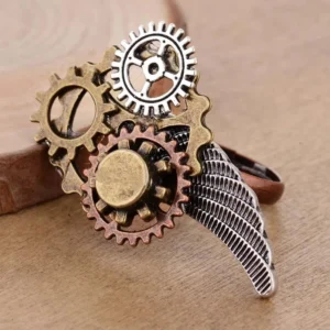 Steampunk wing gear ring with textured silver wing and multi-layer stacked gears, shown in left 3/4 view on wooden table - vintage mixed metal finish statement jewelry