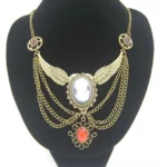 Steampunk winged cameo necklace with antiqued brass finish and red teardrop gem pendant, displayed on black jewelry mannequin bust against white studio background