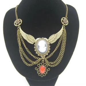 Steampunk winged cameo necklace with antiqued brass finish and red teardrop gem pendant, displayed on black jewelry mannequin bust against white studio background