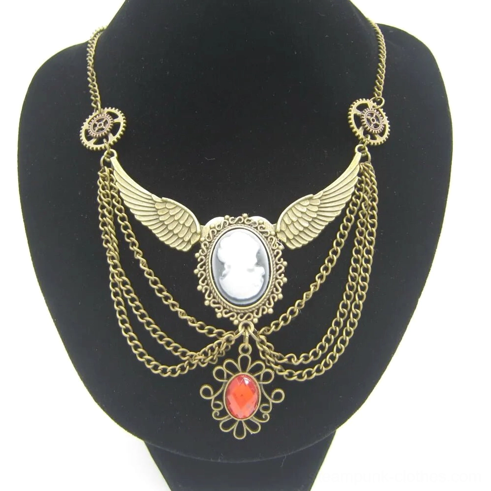 Steampunk winged cameo necklace with antiqued brass finish and red teardrop gem pendant, displayed on black jewelry mannequin bust against white studio background