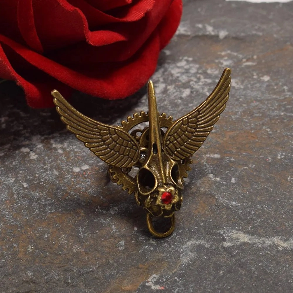 Steampunk winged skull ring with crimson gem and intricate gear details, antique bronze finish on textured stone surface with red rose