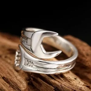 Wrench steampunk ring side view showing dual wrench design with polished silver metal and engraved decorative details on weathered wood surface