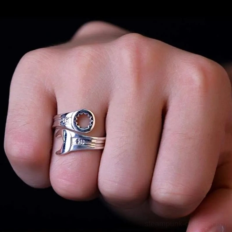 Male hand wearing industrial wrench steampunk ring on middle finger showing gear opening design and polished finish against dark background