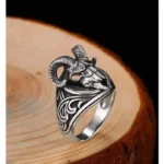Sterling silver ram skull steampunk ring three-quarter view showing curved horns and scroll engravings on dark wooden background