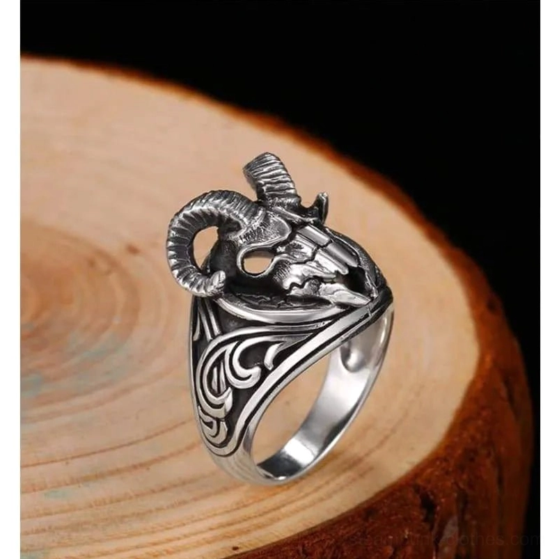 Sterling silver ram skull steampunk ring three-quarter view showing curved horns and scroll engravings on dark wooden background