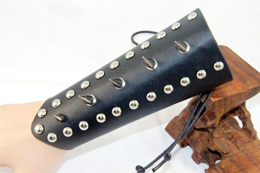 Spiked studded black leather wrist armor with mixed round and teardrop metal studs, angled side view displayed on wooden display stand