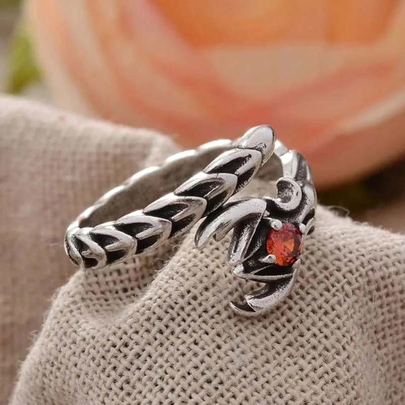 Two-tone silver-black steampunk scorpion ring with red gemstone and wrap-around design on linen backdrop - top-down side angle