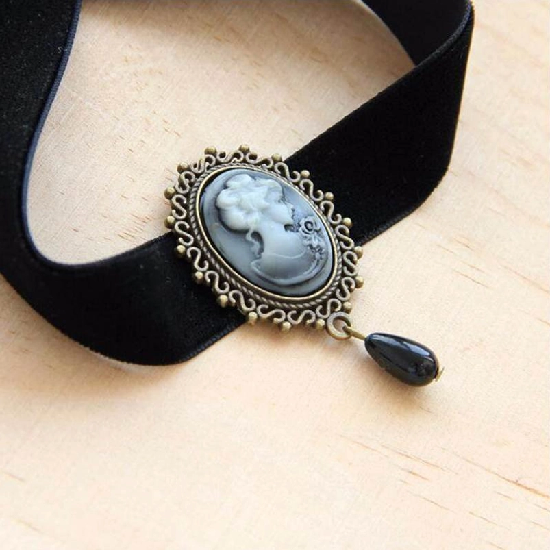 Close-up detail of Victorian velvet choker showing black velvet band, detailed bronze filigree frame, and grey portrait cameo on wooden surface