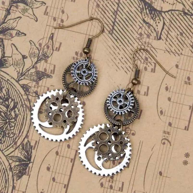 Two-tone steampunk gear earrings with bronze ear hooks displayed on vintage sheet music and floral pattern background, dangling earrings design from oblique angle