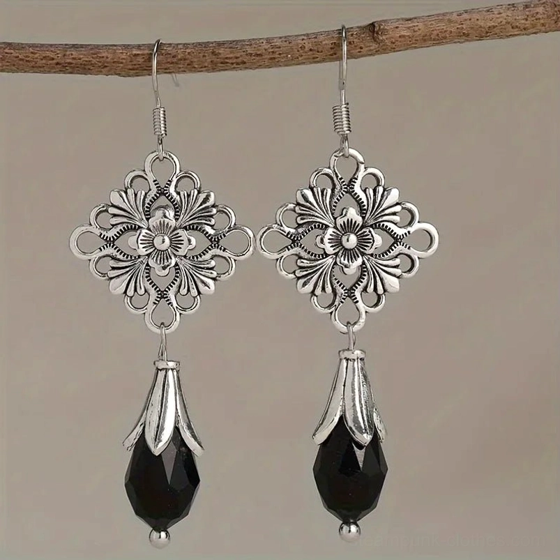 Vintage silver flower drop earrings with ornate filigree design and black crystal pendant, hanging on wooden branch front view