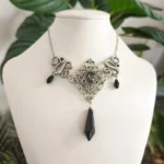 Victorian Gothic snake choker necklace with black faceted gemstones, silver-tone antique finish metal with intricate filigree and carved serpent detail, displayed on white jewelry mannequin against green foliage background