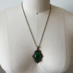 Victorian emerald green pendant necklace with antique bronze ornate frame and oval cabochon stone displayed on dress form mannequin front view