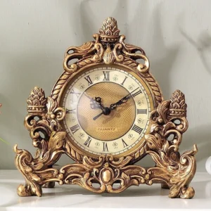 Victorian steampunk desktop clock with ornate bronze-golden carved resin frame and Roman numeral dial, front view on gray wall background