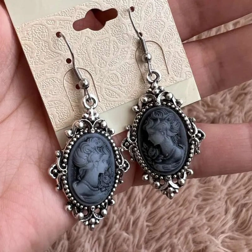 Victorian cameo earrings held on display card showing delicate silver trim and dark grey female cameo profile in overhead lighting