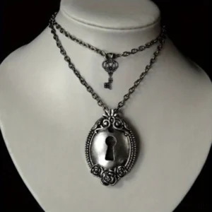 Vintage lock and key layered steampunk necklace with antique silver-tone pendant and matching mini key charm on cloth mannequin against dark studio backdrop