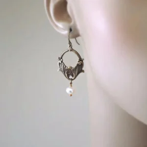 Single vintage pearl drop earring on mannequin ear showing intricate filigree brass design and white pearl charm with gold accents in close-up side view