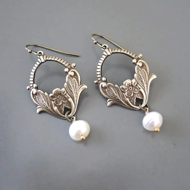 Pair of vintage pearl drop earrings with antiqued brass filigree and carved floral motifs, displayed in flat lay on gray background