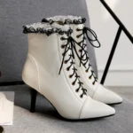 White steampunk Victorian lace-up heeled ankle boots with black ruffled lace trim, pointed stiletto toe, and gold-toned lace eyelets - three-quarter side view