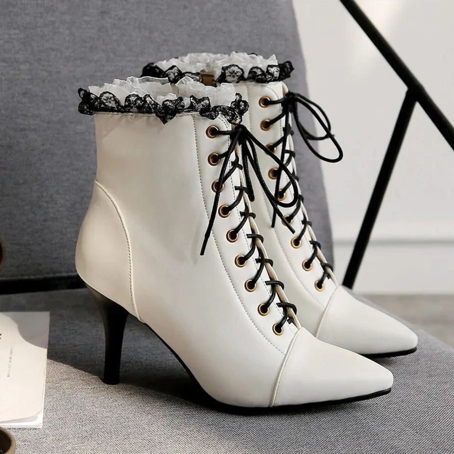 White steampunk Victorian lace-up heeled ankle boots with black ruffled lace trim, pointed stiletto toe, and gold-toned lace eyelets - three-quarter side view