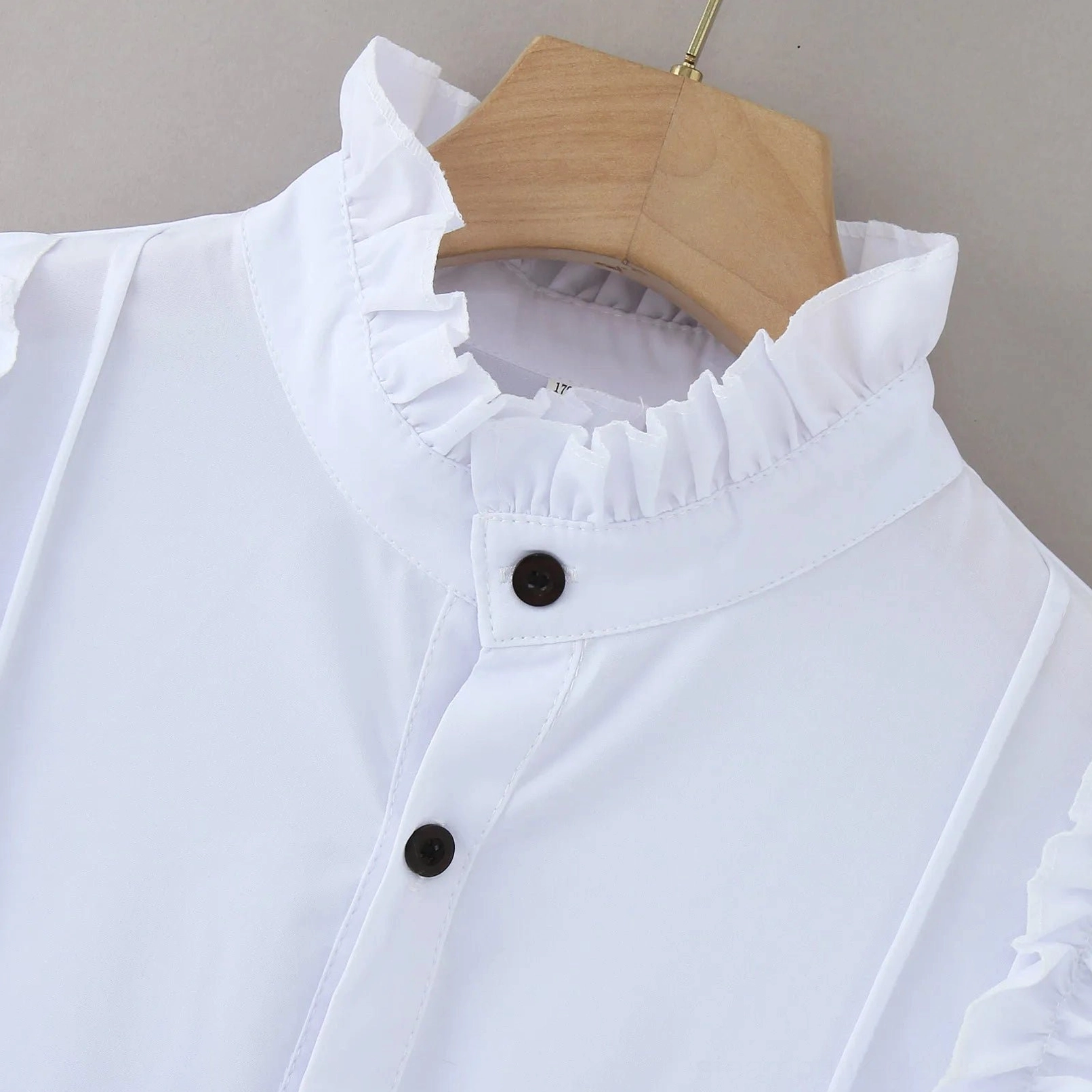 Ruffled stand collar and upper placket detail of white steampunk Victorian shirt on wooden hanger