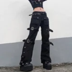 Women's black steampunk cargo pants with silver buckles worn by model in outdoor setting, featuring low-rise design and side snap fasteners